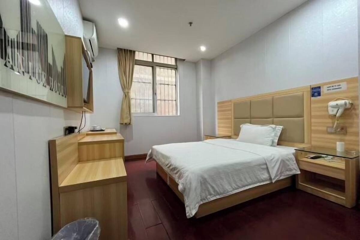 Une chambre d’hôtel équipée d’un lit, d’un bureau, d’une chaise, d’une fenêtre avec des rideaux et d’un climatiseur fixé au mur.