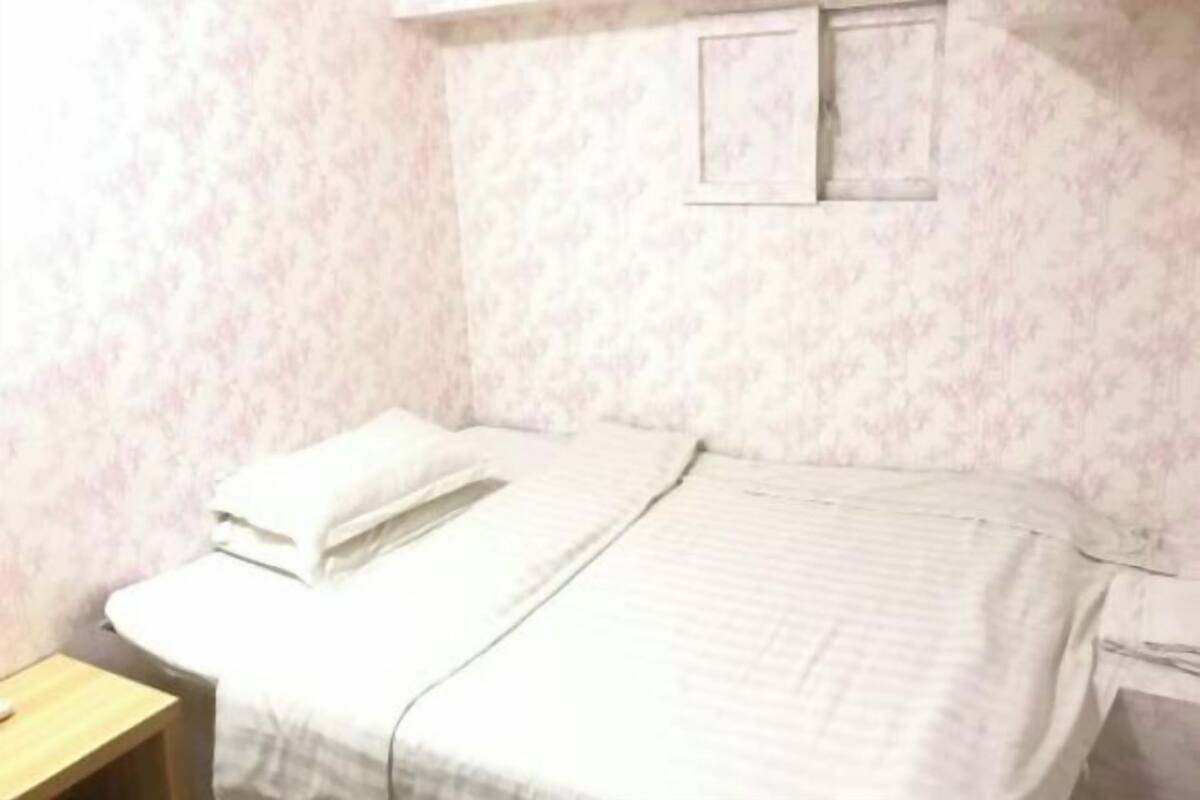 Un lit simple avec une couvre-lit et des oreillers blancs, une table de chevet en bois et une petite table avec une chaise.