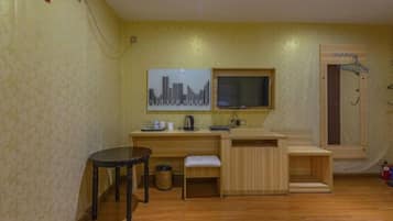 A compact room with a wooden floor, a small table, a bench, a TV mounted on the wall, and a window with a view.