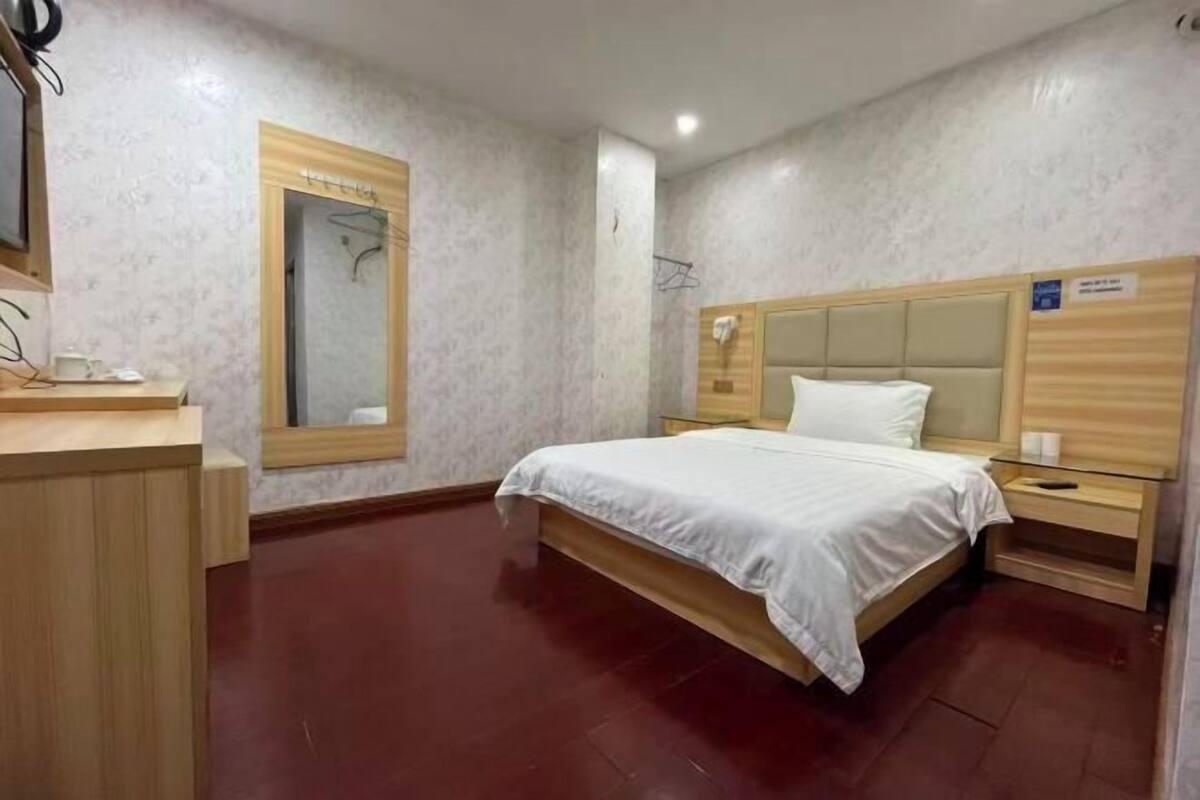 Une chambre d’hôtel avec un lit, des tables de chevet en bois, un miroir et une armoire en bois.