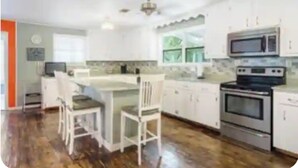 A kitchen with white cabinets, a central island with chairs, and built-in appliances including a microwave and oven.