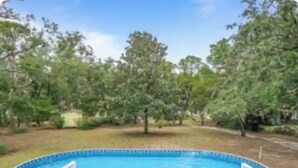 A swimming pool with a wooden deck and lounge chairs, surrounded by trees.