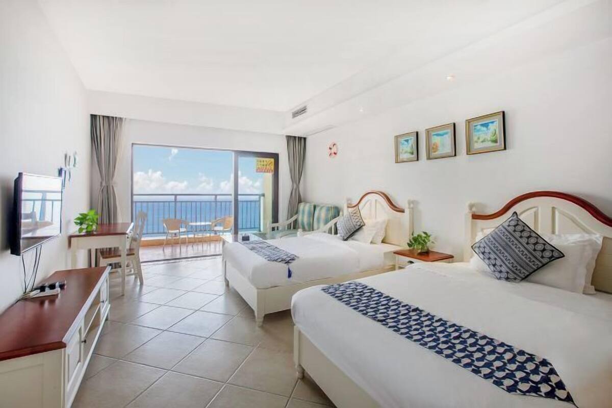 Une chambre d’hôtel avec deux lits, un bureau, une chaise, une télévision et un balcon avec vue.