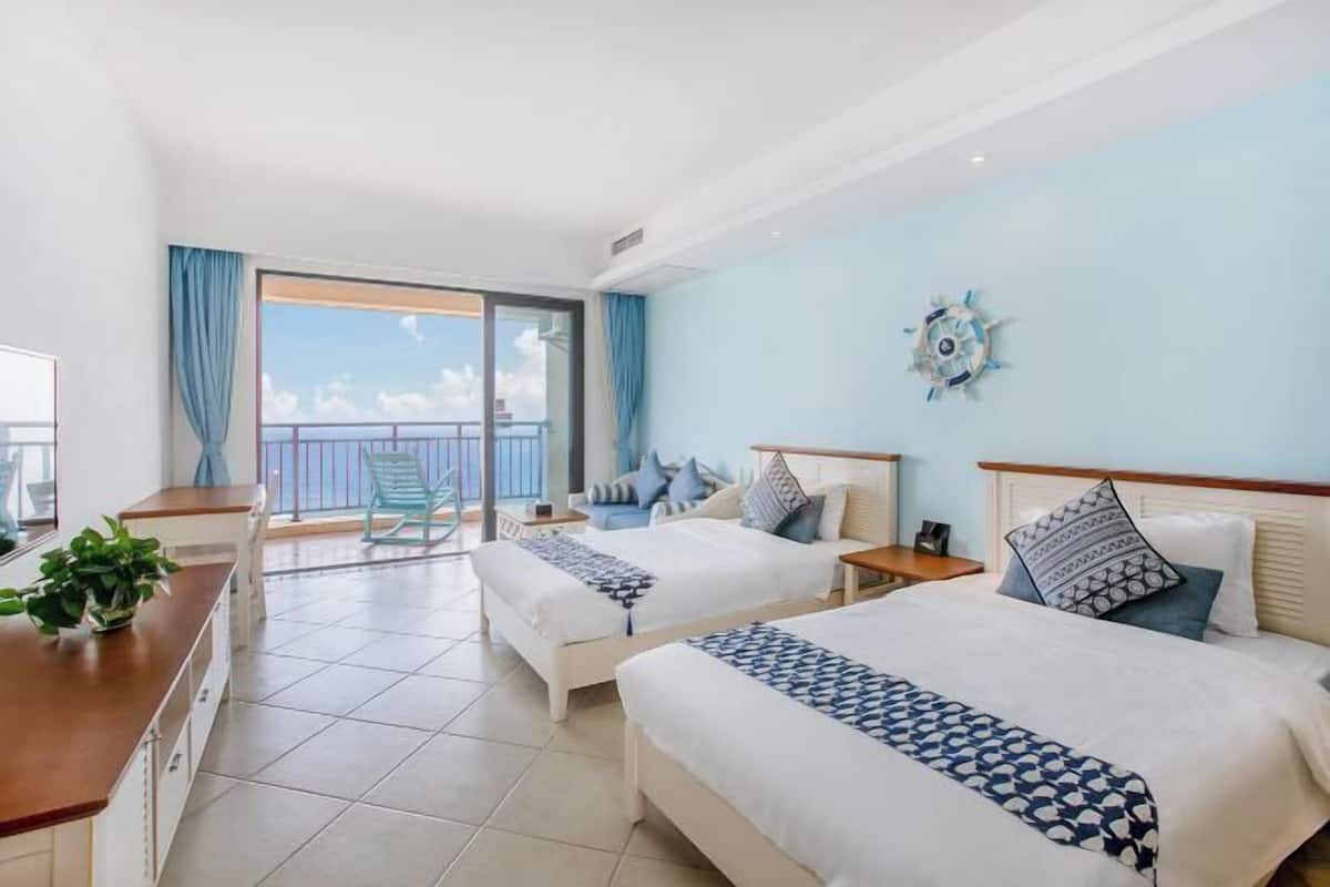 Une chambre d’hôtel avec deux lits, un balcon offrant une vue, un petit bureau et une plante en pot.