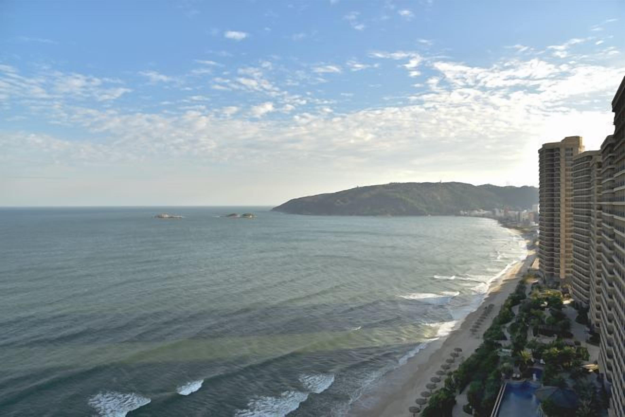 Un hotel frente al mar con vistas al océano y la playa, que cuenta con una estructura de gran altura y una zona ajardinada.