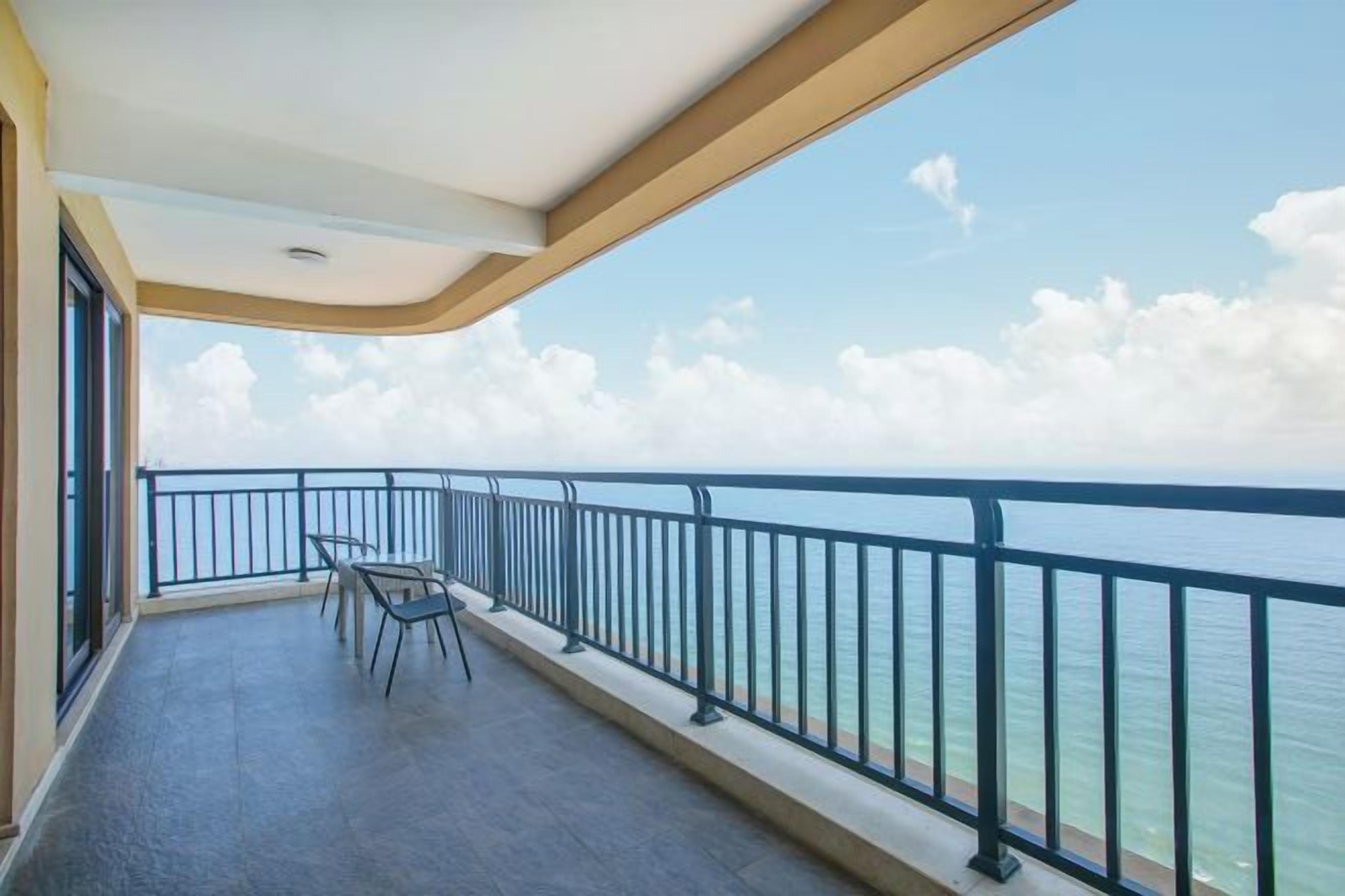 Un balcón con vista al mar, barandilla y una mesa con sillas.