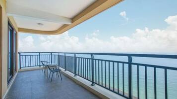 Un balcón con vista al mar, barandilla y una mesa con sillas.