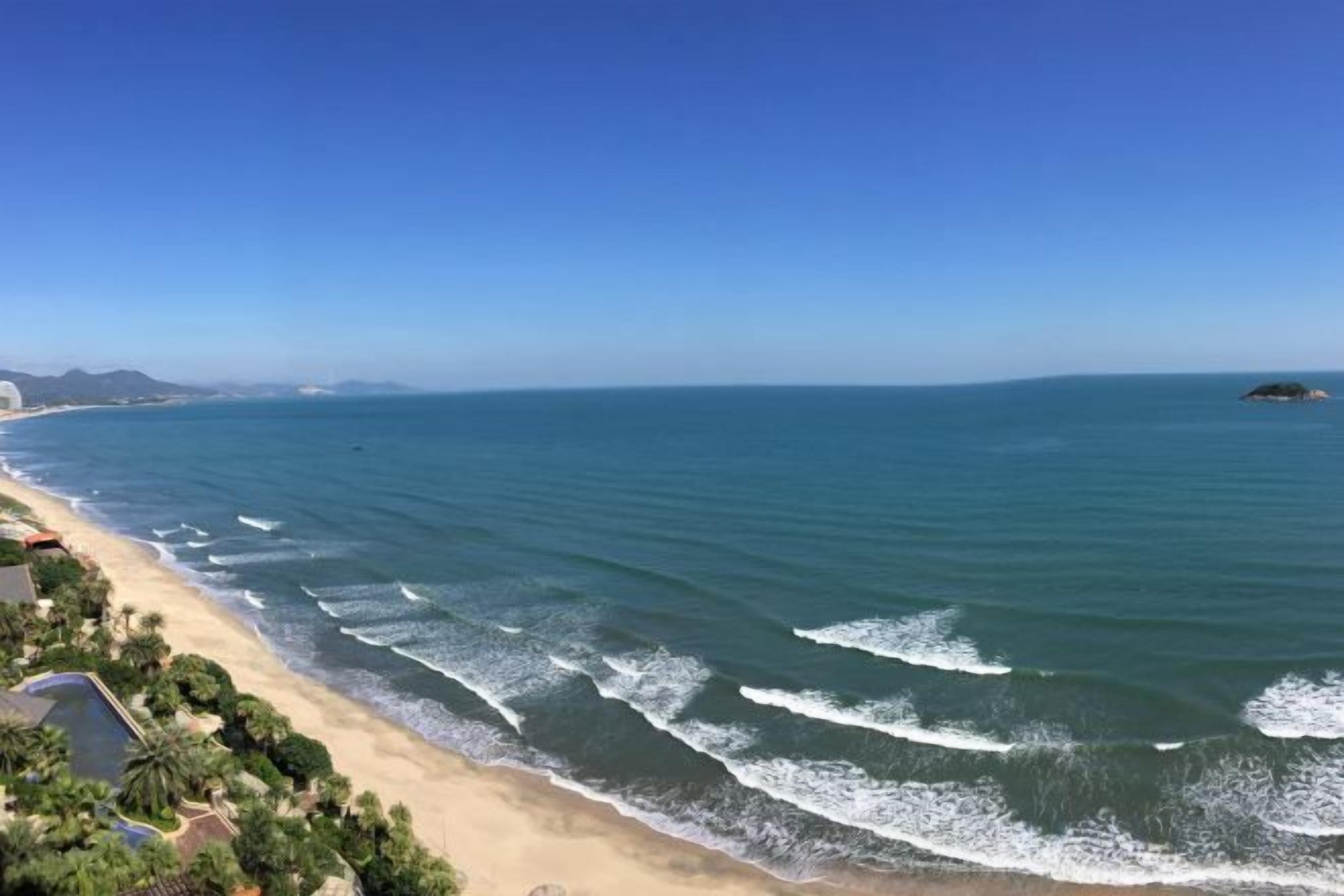Una playa costera con olas, cielo despejado y tierra a lo lejos.