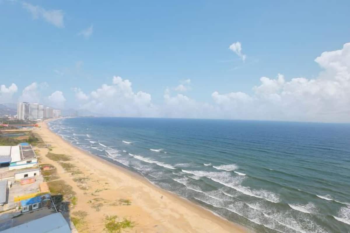 Une vue sur la côte, avec une plage de sable, des vagues de l’océan et des bâtiments le long du rivage.