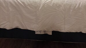 Una cama bien hecha con una toalla blanca doblada, un almohadón oscuro y una mesita de noche con una lámpara.