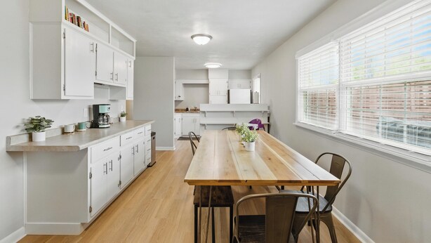Una cocina moderna con armarios blancos, una mesa de comedor de madera y una ventana con persianas.