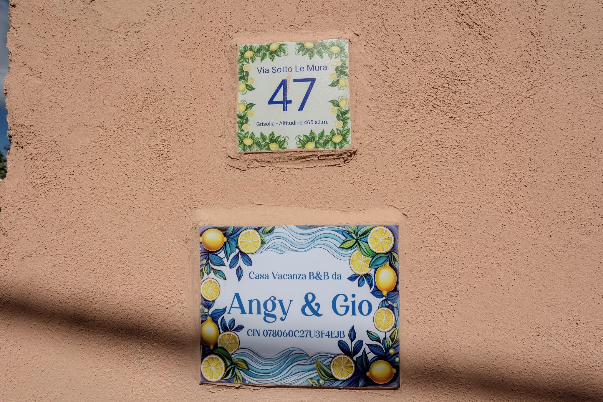 Dos letreros en una pared con textura: uno muestra un número de dirección, y el otro el nombre de la propiedad con información de contacto.