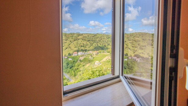 A room with a large window offering a view of a hillside with buildings.