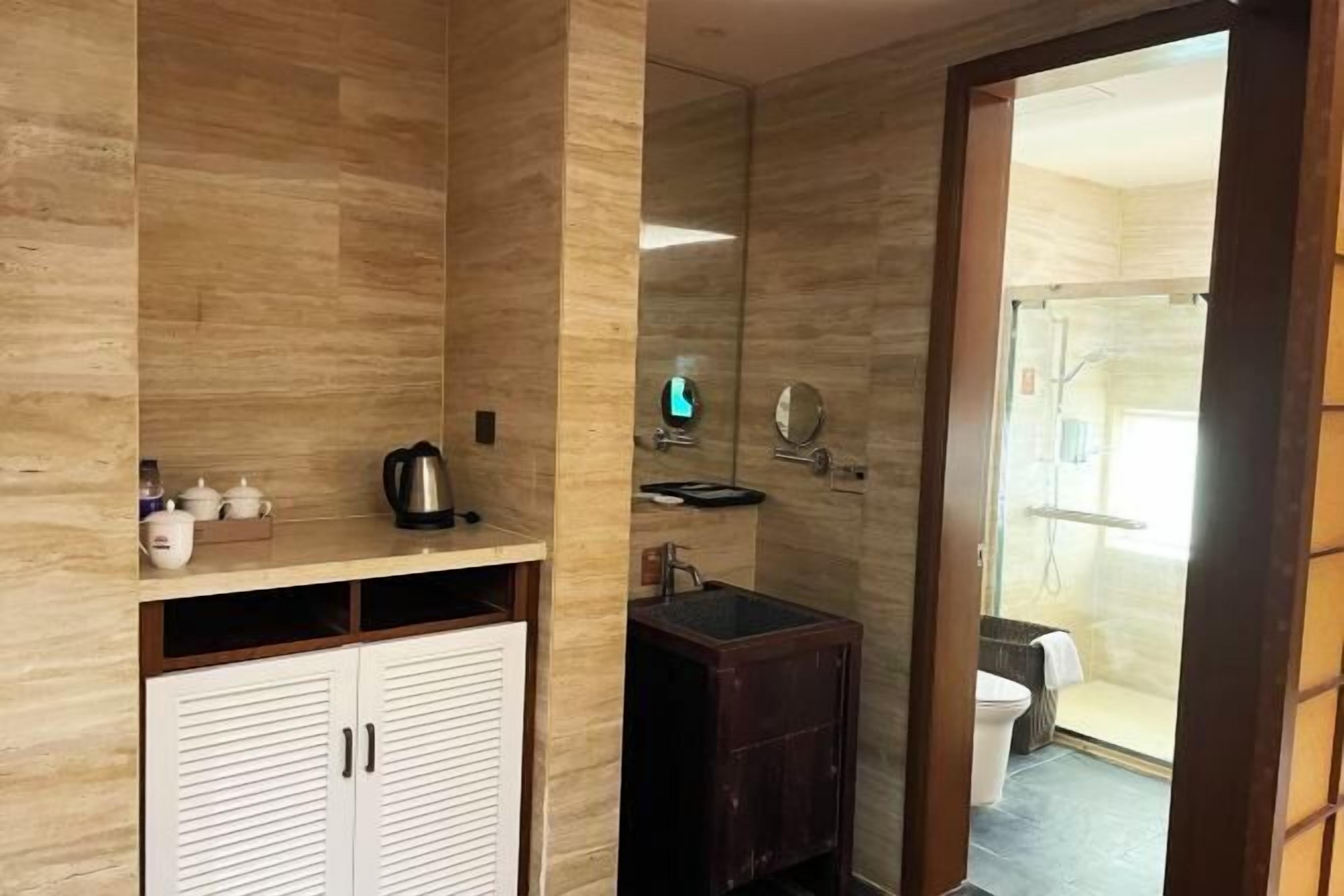 Ein Badezimmer mit einem Holzbadezimmer-Möbel, einem Waschbecken und einem Spiegel. Eine Duschkabine ist durch eine Glastür sichtbar.