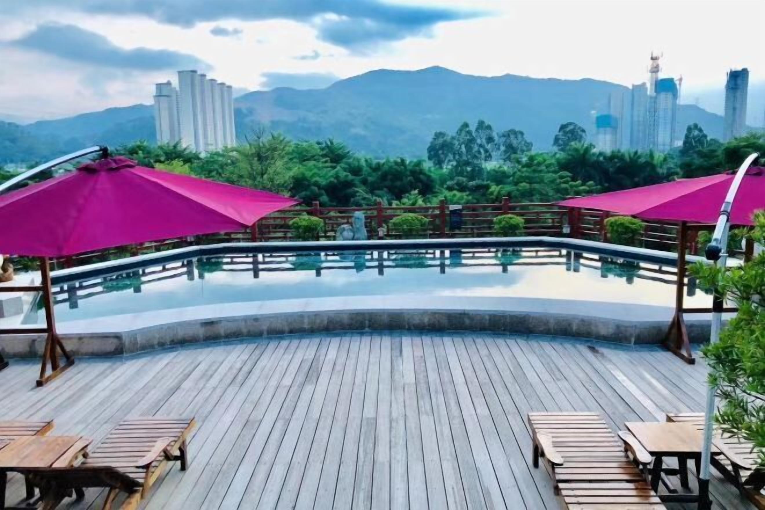 A wooden deck with a pool, surrounded by greenery and a cityscape in the background.
