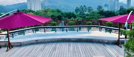 A wooden deck with a pool, surrounded by greenery and a cityscape in the background.