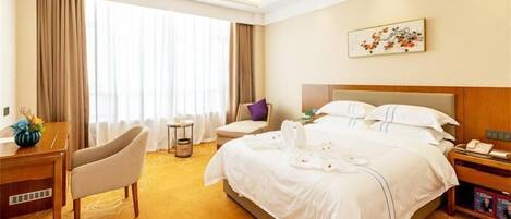 A hotel room with a large bed, a desk with a chair, a small table, and a nightstand.