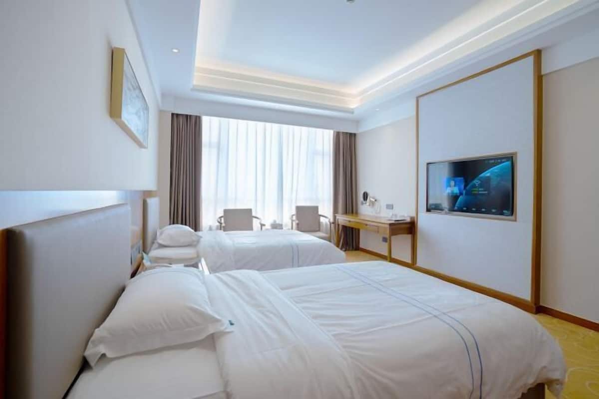 Quarto de hotel com duas camas, uma escrivaninha, televisão e uma janela grande com cortinas.