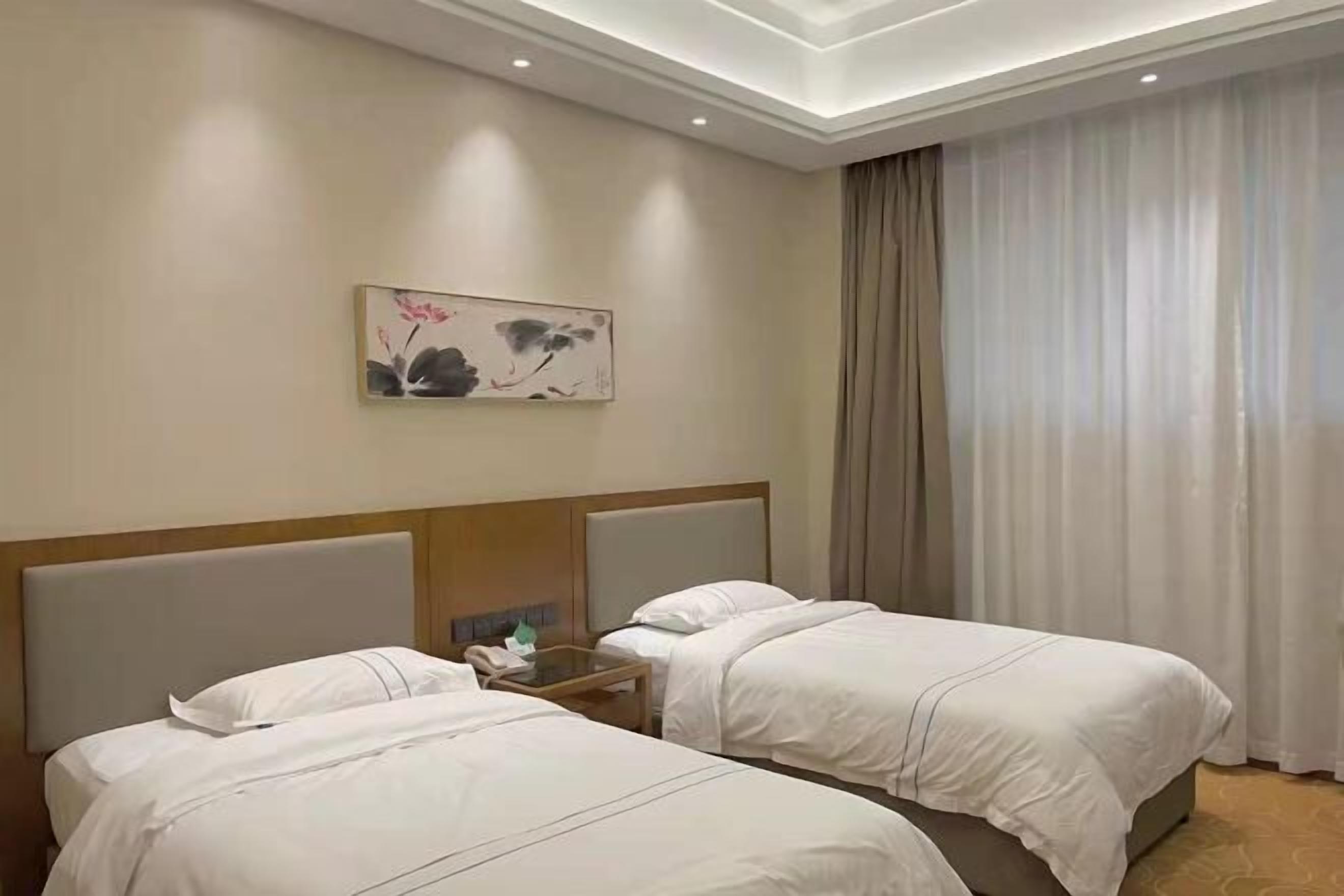 Una habitación de hotel con dos camas, una mesita de noche con un teléfono, un cuadro en la pared y un amplio ventanal con cortinas.