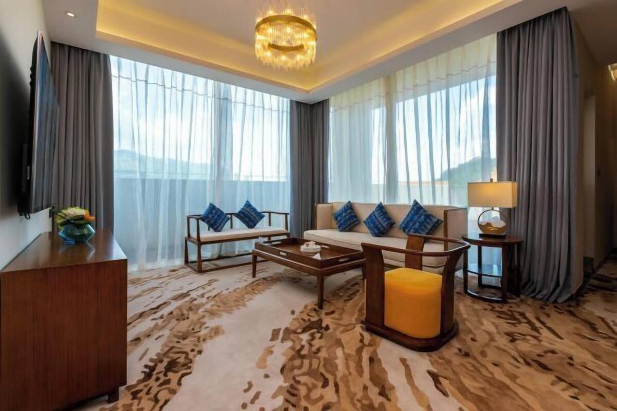 Quarto de hotel moderno com sofá, mesa de centro, televisão e luminária.