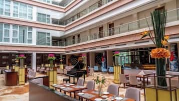 A multi-level hotel lobby with a grand piano, dining tables, and a central fountain.