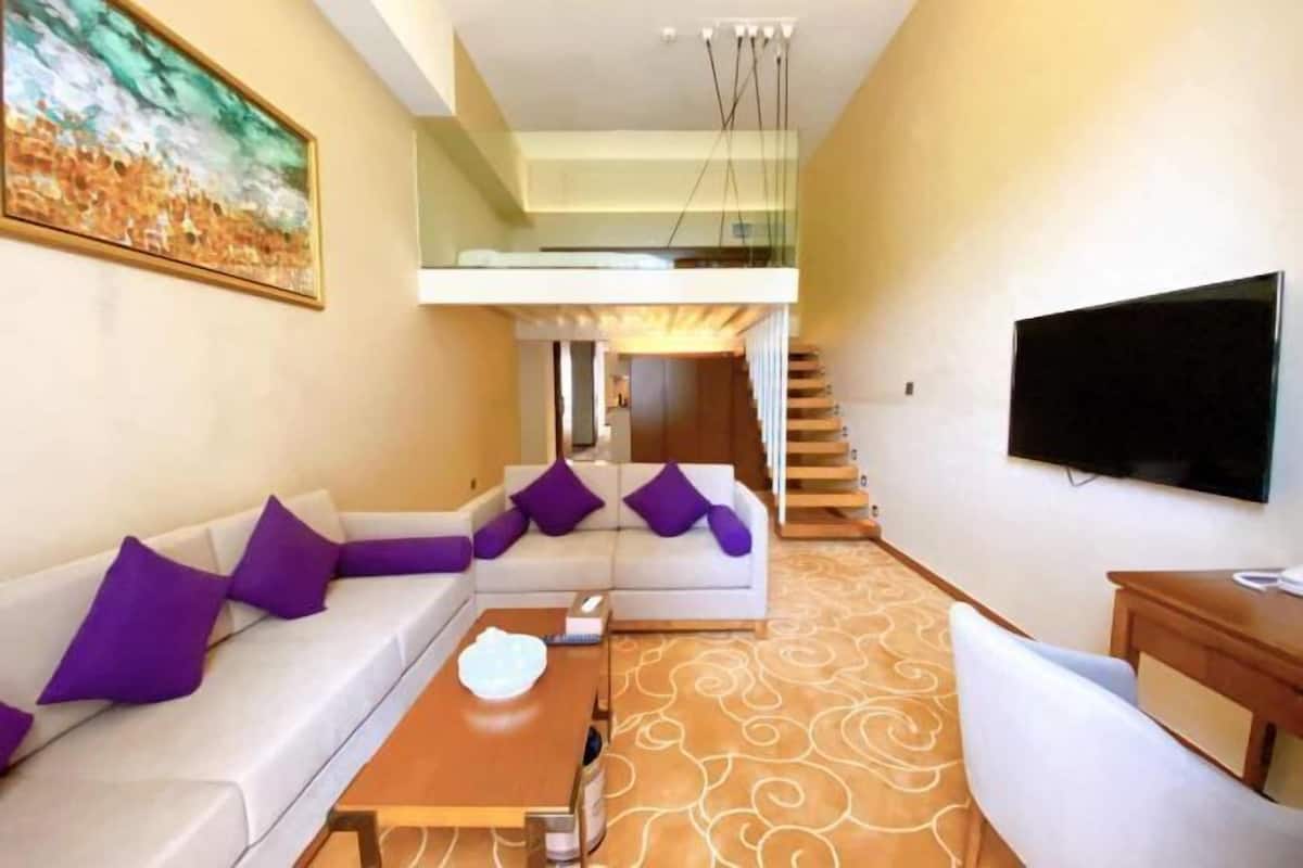 Uma sala de estar moderna com um sofá seccional, uma televisão de tela plana e uma escada que leva a um andar superior.