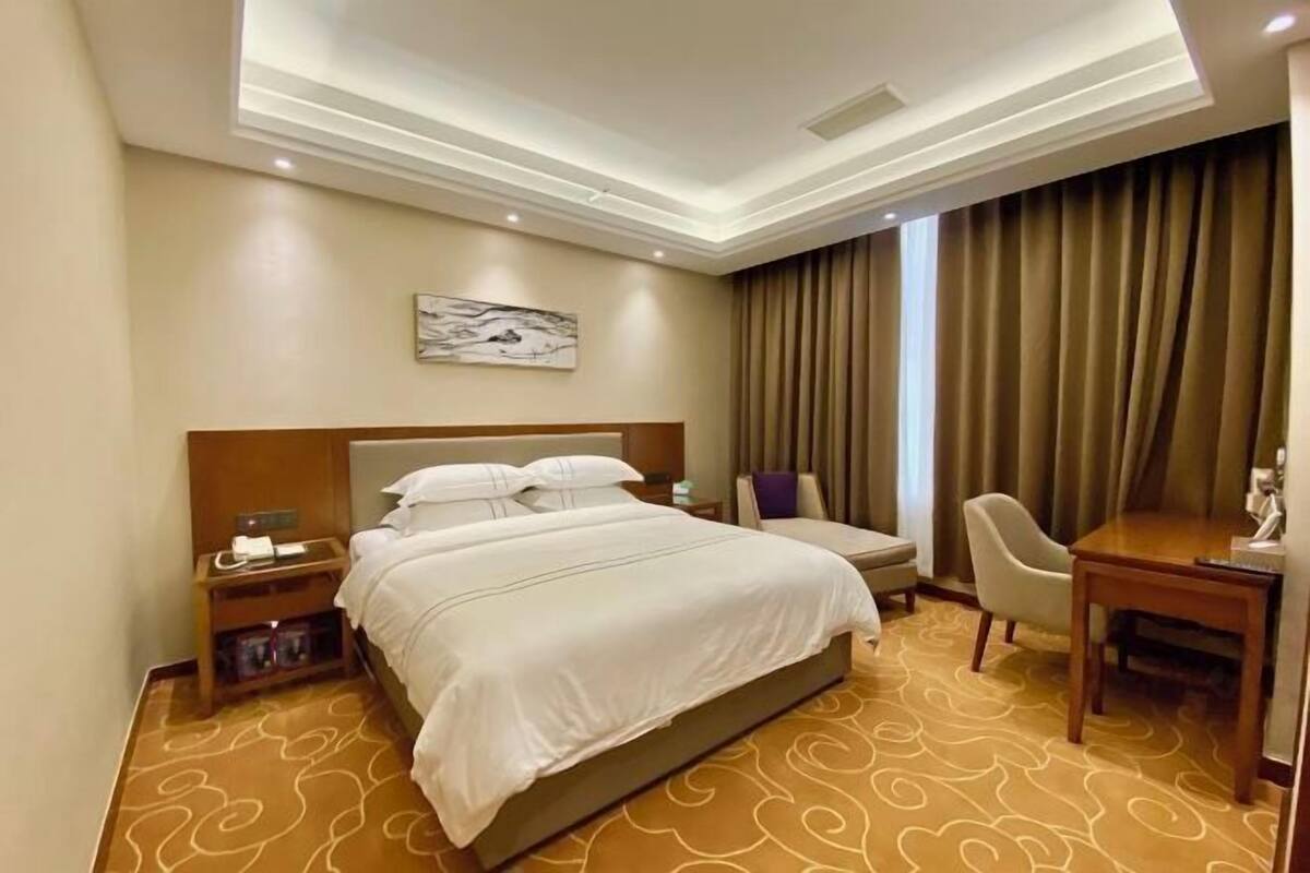 Quarto de hotel com uma cama grande, uma escrivaninha, uma cadeira e uma mesa de cabeceira.