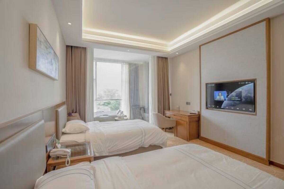 Quarto de hotel com duas camas, uma escrivaninha, uma televisão e uma janela com cortinas.