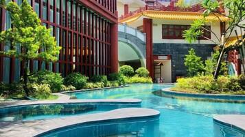 A swimming pool area with a modern building, greenery, and a traditional architectural element.