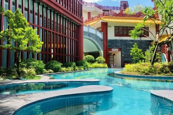 A swimming pool area with a modern building, greenery, and a traditional architectural element.