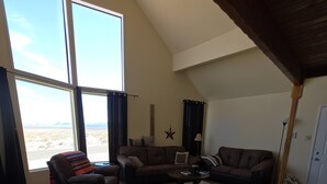 A spacious living room with a large window, a sectional sofa, a small coffee table, and a wooden floor.
