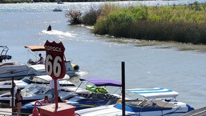 A marina with boats docked, a sign reading "Topock 66", and a view of a river and hills in the background.