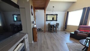 A spacious living area with a wooden ceiling, a dining table with chairs, a sofa, and a TV on a wooden cabinet.