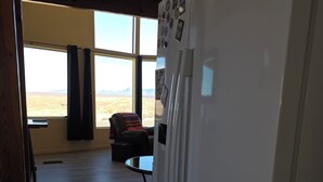 A kitchen with a white refrigerator, wooden flooring, and a view of a desert landscape through large windows.