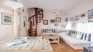 Un salón acogedor con un sofá blanco, cojines a rayas, una mesa de centro de madera y una escalera en espiral.