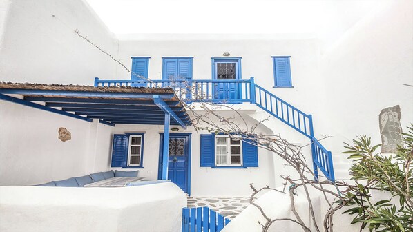Un edificio bianco con porte e persiane blu, una scala e un pavimento in pietra.
