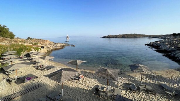 Una playa con aguas cristalinas, sombrillas y un faro a lo lejos.