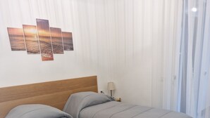 A hotel room with two beds, a wooden headboard, a wall-mounted lamp, and a window with sheer curtains. - 3-bedroom apartment in gorgeous Dizzasco with WiFi (Dizzasco)