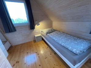 Una habitación pequeña con una cama individual, paredes de madera y una ventana.