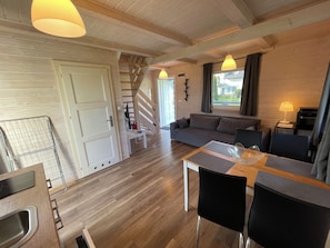 Un interior moderno con suelo de madera, un sofá, una mesa de comedor con sillas y una escalera.