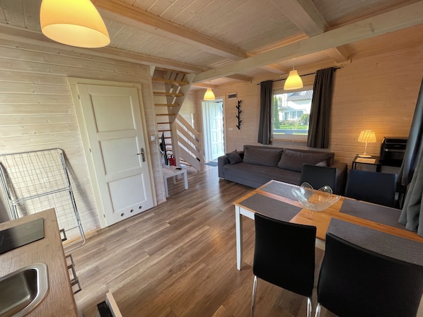 Un interior moderno con suelo de madera, un sofá, una mesa de comedor con sillas y una escalera.