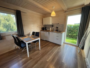 Una cocina moderna con suelo de madera, una mesa de comedor con sillas, un horno empotrado y un ventanal con cortinas.
