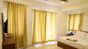 Una habitación de hotel con cama, mesita de noche, espejo y cortinas amarillas.