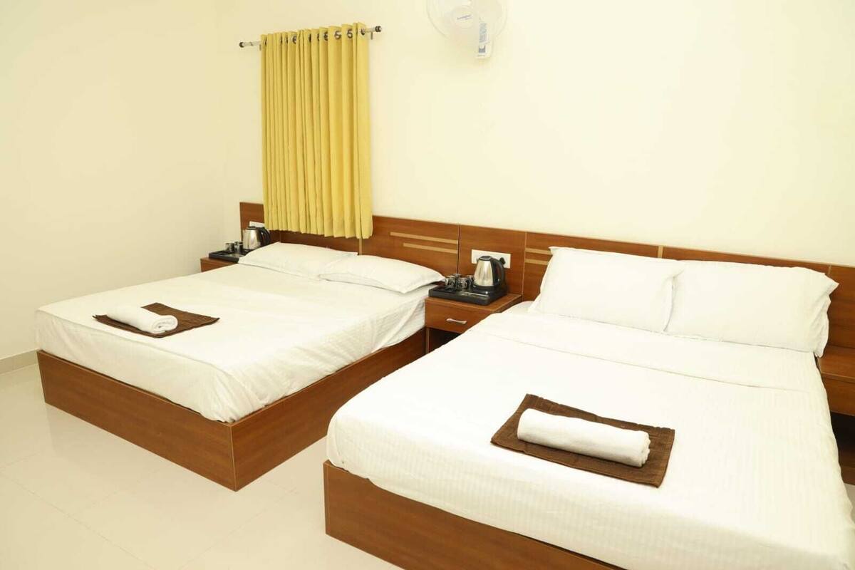 Ein Hotelzimmer mit zwei Einzelbetten, jeweils mit einem Holz-Kopfteil, weißer Bettwäsche und einem braunen Handtuch auf dem Bett. Ein Nachttisch mit Wasserkocher und Tasse steht daneben.