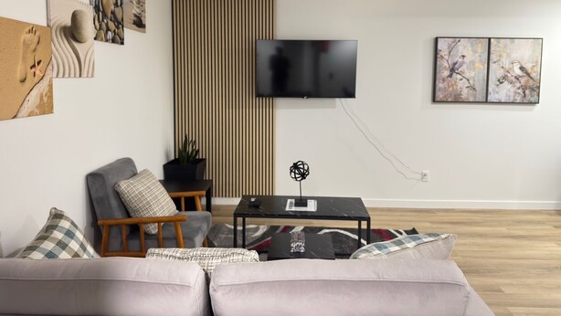 A modern living room with a sofa, a coffee table, and a flat-screen TV mounted on the wall.