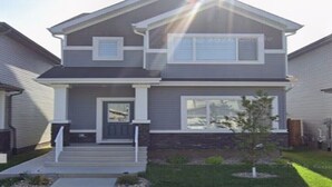 A two-story residential house with a front porch, a small front yard, and a visible garage door.