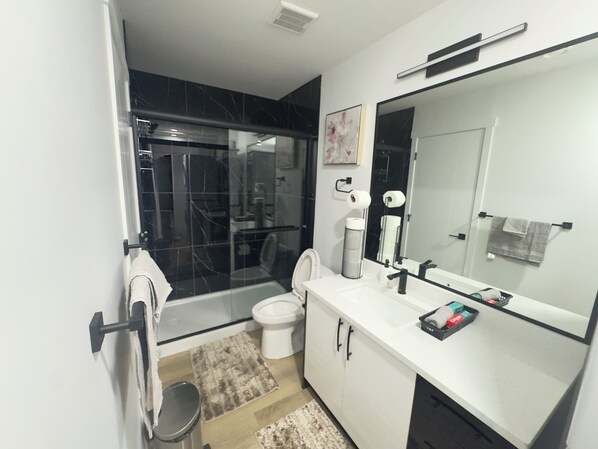 Un baño moderno con cabina de ducha de vidrio, inodoro blanco y un espejo grande sobre el lavamanos.