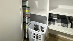 A laundry basket in a closet with shelves and a striped towel.