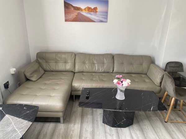 A modern living room with a beige sectional sofa, a black marble coffee table, and a wooden floor. - 3 Bedroom House- Loughborough-sleeps 5-freeparking (Loughborough)