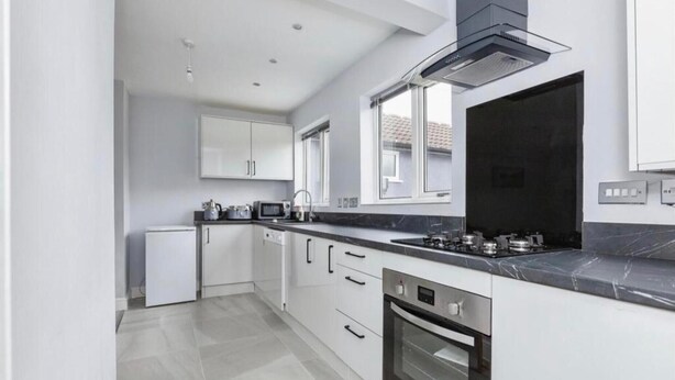 A modern kitchen with white cabinets, a black countertop, and stainless steel appliances. - 3 Bedroom House- Loughborough-sleeps 5-freeparking (Loughborough)